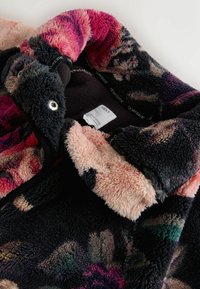 Kurtka polarowa z wzorem kwiatowym w ciemnych kolorach z różowymi i beżowymi akcentami. Miękka tekstura, czarna podszewka wewnętrzna oraz widoczne markowe metki.