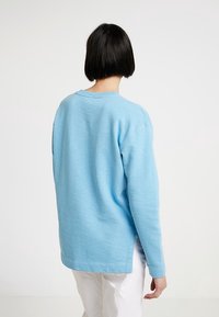 Sudadera de manga larga azul claro con un corte relajado, escote redondo y aberturas laterales en el dobladillo. Fabricada en tela suave y texturizada.