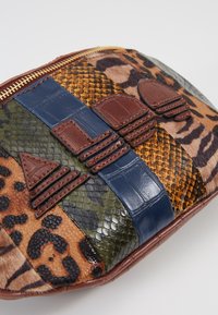 Pochette patchwork avec imprimés animaux mixtes et textures en tons de marron, bleu, vert et orange, ornée d'accents décoratifs en cuir marron.