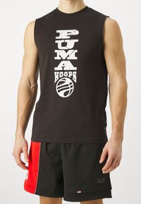 Černé bezrukávové tričko s bílým potiskem "PUMA HOOPS" a ikonou basketbalu. Nosí se s černými síťovanými šortkami s červenými akcenty a logem.