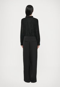 Haut noir texturé à manches longues avec taille et col froncés, associé à un pantalon noir taille haute à jambes larges avec poches arrière.