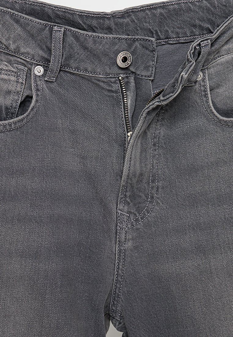 Jeans en denim gris avec fermeture éclair, bouton en métal et poches avant. Tissu texturé avec des détails de couture visibles.