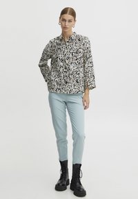 Zwart-wit gestreepte button-up shirt met driekwartmouwen, gecombineerd met lichtblauwe slim-fit broek en zwarte veterlaarzen.