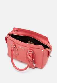 Sac à main en cuir corail avec une surface texturée, accents en métal argenté, deux poignées et un haut zippé. Présentant une marque sur le devant.