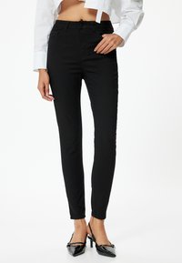 Vaqueros skinny negros hechos de una mezcla de algodón. Presentan un diseño clásico de cinco bolsillos y una cintura de altura media. Textura suave, ajuste hasta el tobillo.