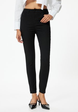 Jean skinny noir en mélange de coton. Présente un design classique à cinq poches et une taille mi-haute. Texture lisse, coupe à la cheville.