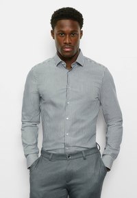 Gestreiftes Hemd mit Knopfleiste in Weiß und Marineblau, langärmlig, klassischer Kragen. Schmale Passform mit glatter Textur. Graue Hose mit Fronttaschen.