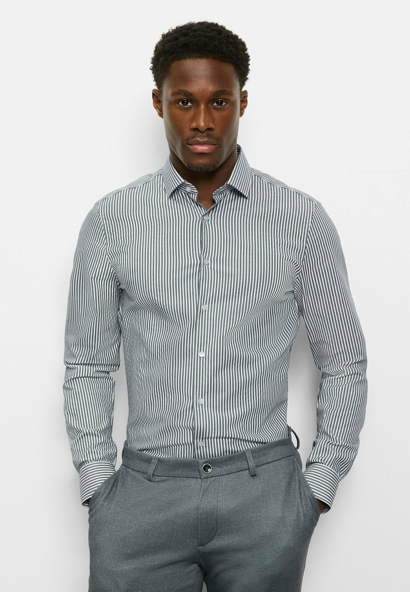 Gestreiftes Hemd mit Knopfleiste in Weiß und Marineblau, langärmlig, klassischer Kragen. Schmale Passform mit glatter Textur. Graue Hose mit Fronttaschen.