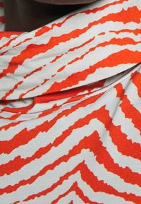 Röd och vit randig tyg med ett abstrakt zigzag-mönster, med en mjuk textur och en draperad halsdesign.