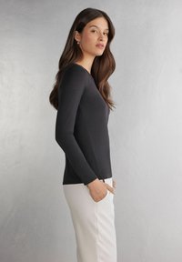 Schwarzes Langarmtop aus dehnbarem Stoff, mit rundem Ausschnitt und figurbetonter Silhouette, kombiniert mit weißen Hosen.