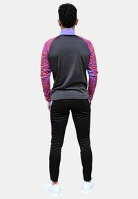 Chaqueta deportiva de color gris oscuro con mangas estampadas en púrpura y rosa, combinada con pantalones negros. El material parece suave y tiene un diseño ajustado.