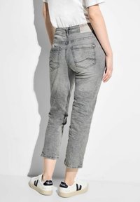 Jeans in denim grigio con una texture sbiadita, vita media e gambe tapered. Presentano tasche posteriori e un'etichetta del marchio visibile sulla vita.