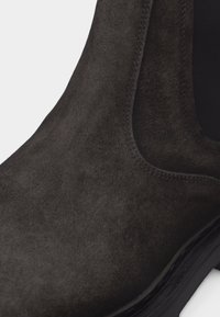 Κοντινή λήψη ενός τσέλσι μποτάκι από σκούρο καφέ σουέτ που δείχνει τη ραφή, το ελαστικό πλαϊνό πάνελ και τη μαύρη σόλα.