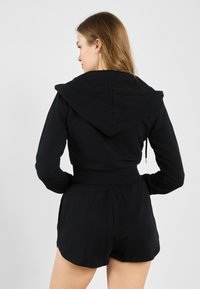 Čierna mikina s kapucňou a skráteným strihom, dlhé rukávy a zodpovedajúce šortky. Vyrobené z mäkkej, elastickej tkaniny s elastickým pásom.
