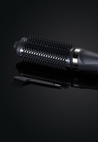 Ronde zwarte haarborstel met rubberen pinnen, gepolijst metalen band en een matte handgreep. Dichtbij ligt een kleine zwarte kam met een puntige uiteinde.