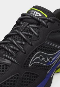 Μαύρο παπούτσι για τρέξιμο Saucony με αντανακλαστικά κορδόνια, επάνω μέρος από δίχτυ, και μπλε με νέον πράσινες πινελιές στη σόλα και το λογότυπο.