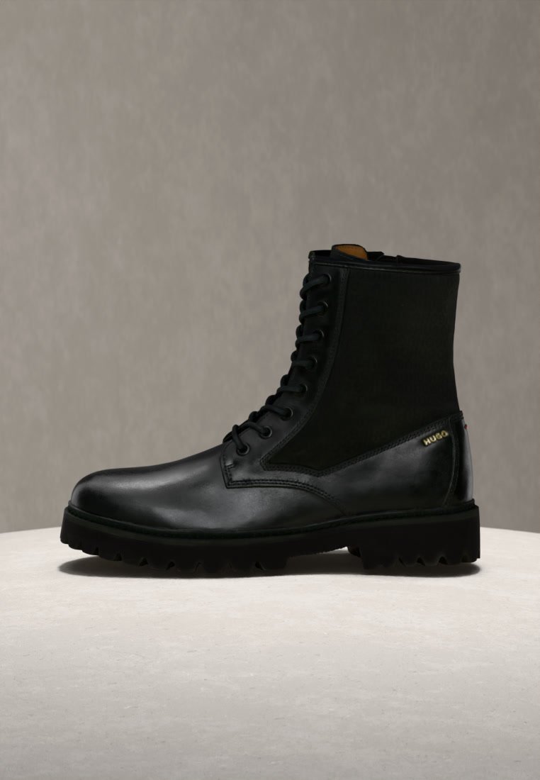 Bottine noire en cuir et suède à lacets avec une semelle robuste, présentée sur une surface claire avec un fond neutre.