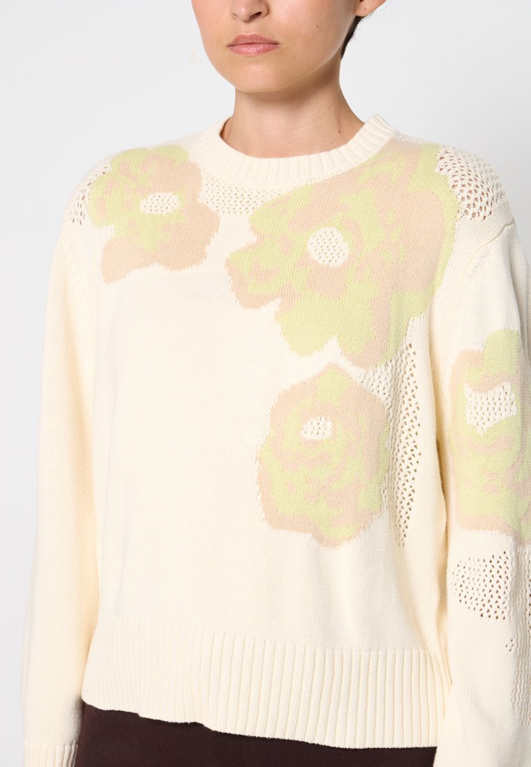 Cremfarbener Pullover mit übergroßen Blumenmustern in zartem Grün und Pfirsich. Mit geripptem Saum und offenem Strickdetail an den Schultern.