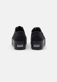 Sorte kanvas-sneakers med tykk gummisåle, bakmerke og subtil teksturdetaljering. Har klassisk snøredesign og lav profil.