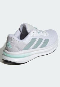 Chaussure de course Adidas blanche et bleu clair avec tissu en mesh, trois bandes latérales, col rembourré et semelle coussinée sur un fond uni.
