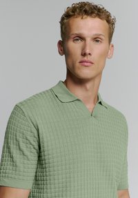 Groene getextureerde polo met korte mouwen, voorzien van een V-hals en een subtiel ruitpatroon. Zacht materiaal en fitted ontwerp.