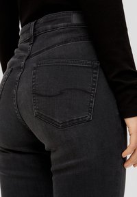 Högmidjade svarta jeans med en figurnära passform. Funktioner inkluderar två bakfickor, subtila sömdetaljer och en slät denimtextur.