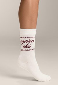 Biały bawełniany skarpet z bordowym dzianym wzorem z napisem "après ski" i dekoracyjną ramką wokół górnej części. Ściągacz na mankiecie.