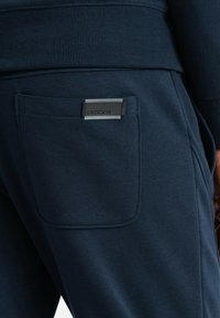 Sudaderas en navy con una cinturilla acanalada, un bolsillo trasero con un parche rectangular de logo negro y una tela suave y texturizada.