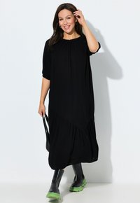 Vestido maxi negro, fluido, con mangas cortas abullonadas y escote recogido. Combinado con botas negras gruesas que tienen suelas verdes.