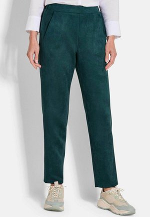 Pantaloni scuro verde, simili al camoscio, con taglio dritto, pieghe frontali e tasche laterali, abbinati a sneakers di colore chiaro.