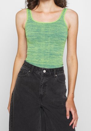 Zielony ryflowany top na ramiączkach z cienkimi paskami, o fakturowanej powierzchni, zestawiony z czarnymi szortami denimowymi z wysokim stanem i detalem w postaci guzika.