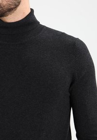Maglione a collo alto nero, realizzato in materiale liscio e a maglia fine. Presenta una forma aderente con un collo a coste e maniche lunghe.