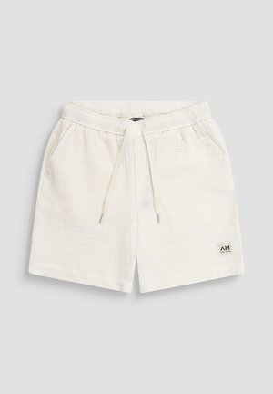 Pantaloncini in tessuto bianco strutturato con vita elasticizzata, coulisse, tasche laterali e una piccola etichetta del marchio sulla gamba sinistra inferiore.