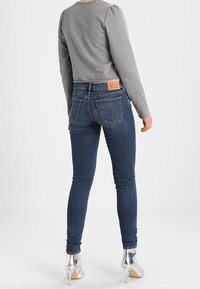 Person wearing dark blue skinny jeans, gray long-sleeve top, and silver high-heeled ankle boots, standing against a plain white background.