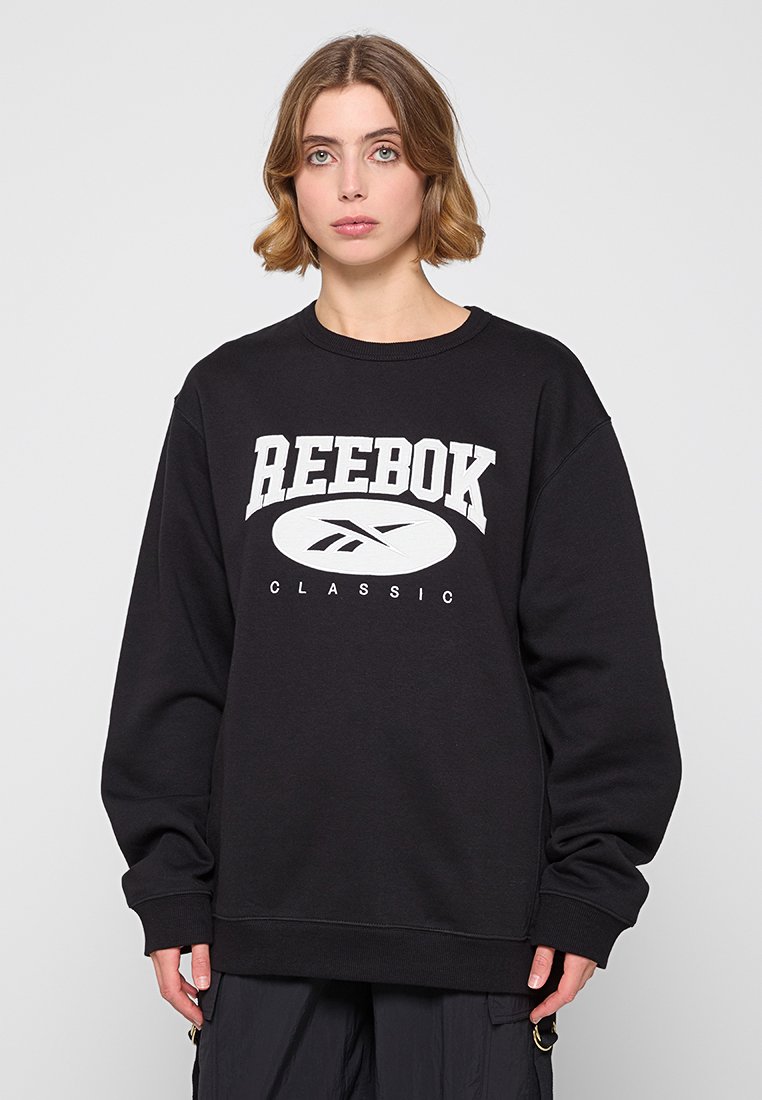 Felpa nera in cotone, con un grande logo Reebok bianco posizionato al centro della parte anteriore. Fit ampio con polsini e vita a coste.