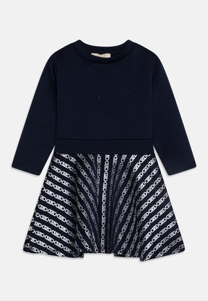 Langærmet mørkeblå kjole med ensfarvet overdel og vid nederdel med hvidt geometrisk kædemønster.