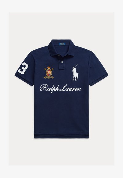 Tengerészkék galléros póló, fehér hímzett logóval, a hüvelyen a 3-as számmal, arany címerrel "20" és