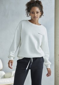 White oversized sweatshirt with ribbed cuffs, featuring a small black logo. Paired with slim-fit black sweatpants with drawstring.