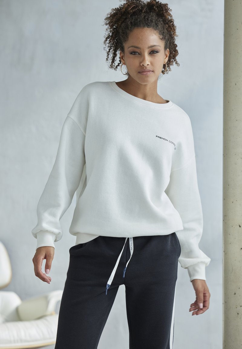 White oversized sweatshirt with ribbed cuffs, featuring a small black logo. Paired with slim-fit black sweatpants with drawstring.