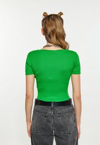 Top verde din tricot cu model striat, cu mâneci scurte, având un decolteu larg și un design scurt, asortat cu blugi negri cu talie înaltă.