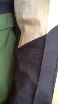 Textured fabric in black, green, and cream colors, featuring an angular, layered design with noticeable contrasting sections.