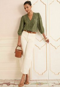 Blouse brodée vert olive avec des manches bouffantes, associée à un pantalon large crème. Les accessoires incluent une ceinture marron et un mini sac seau.