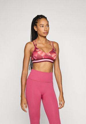 Sportsbh i nyanser av rosa med blomstermønster og tynne stropper; kombinert med høyttalende, ensfargede rosa leggins med en glatt tekstur.