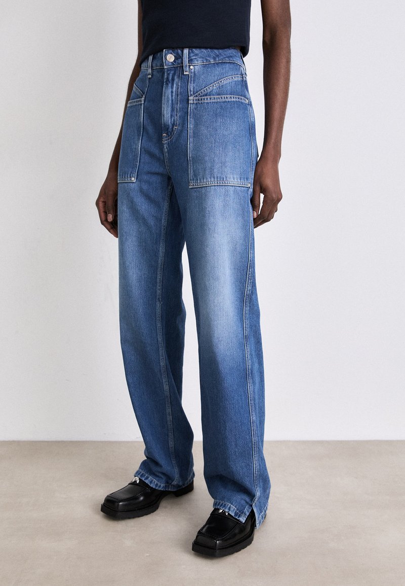 Jeans din denim, de culoare albastru deschis, cu talie înaltă, croială largă și buzunare frontale supradimensionate. Purtați cu încălț�ăminte neagră, cu talpă groasă.