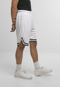 Hvide atletiske shorts med sorte accenter og striber, der har en afslappet pasform og elastisk talje. Båret med hvide sneakers og ankelsokker.