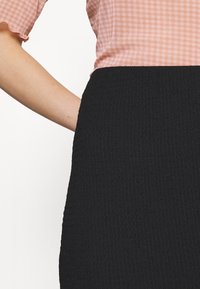 Svart ribbad kjol med texturerad tyg, ihop med en ljusrosa rutiga topp. Toppen har korta, volangärmar.