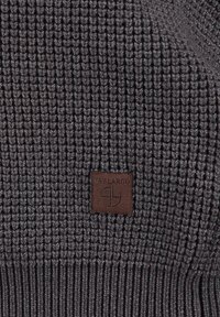 Grauer, gestrickter Stoff mit einem strukturierten Muster; umfasst ein braunes Lederetikett mit "KEY LARGO" und Logo-Details.