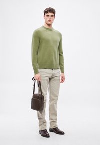 Zöld kötött pulóver, világos bézs farmerek, sötétbarna bőr válltáska és fényes barna cipők, egyszerű, letisztult dizájnnal.