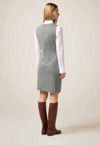 Grau-weißer Hahnentrittmuster-Kleid mit geradem Schnitt, kombiniert mit braunen knielangen Lederstiefeln. Darunter befindet sich ein weißes Hemd.