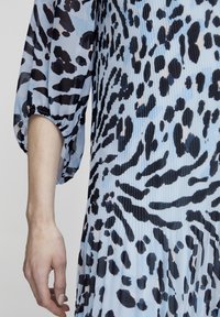 Plava nabrana haljina s apstraktnim leopard printom u crnoj i sivoj boji, s naboranim rukavima i elastičnim manžetama. Glatka tekstura tkanine.